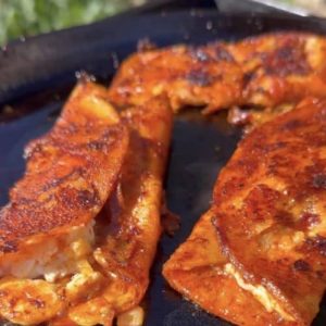 Authentic enchiladas rojas cooking on a skillet, filled with melted cheese and lightly crisped to perfection.