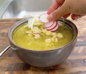 Hand placing sliced radishes over pozole verde.
