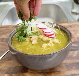 Hand sprinkling chopped cilantro onto pozole verde.