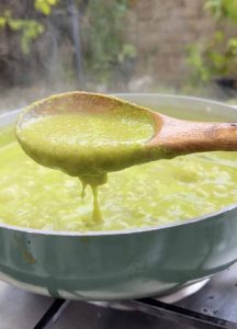 Simmered salsa verde in a pan with a spoon lifting the thickened green sauce for pozole verde.