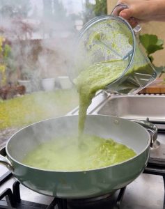 Blended green tomatillo and pepper sauce being poured into a pan to simmer for pozole verde.