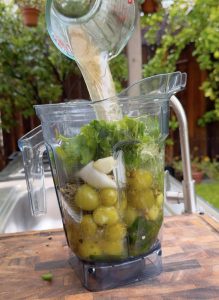 Adding reserved chicken broth to the blender to help blend the green salsa for pozole verde.