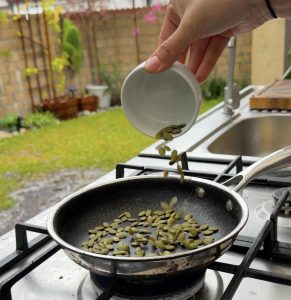Pumpkin seeds being poured into a dry pan for toasting.