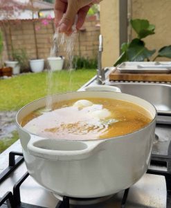 Hand sprinkling salt into the pot of simmering broth.