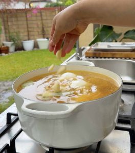 Onion pieces and garlic cloves being added to the broth.
