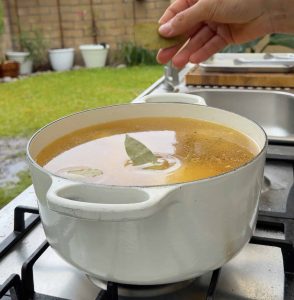 Hand dropping bay leaves into a simmering pot of broth.