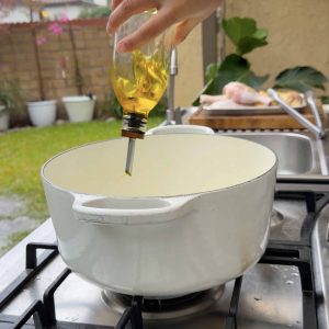 Olive oil being poured into a large white pot on the stove.