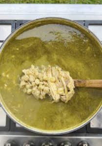 Wooden spoon lifting hominy and chicken from the finished pozole verde.