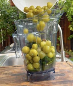Cooked tomatillos being added to the blender with peppers.