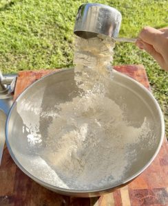 Flour being poured into a large mixing bowl outdoors for making buñuelos de viento.