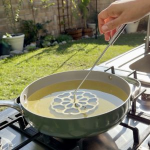 Rosette mold heating inside hot oil before dipping into batter.