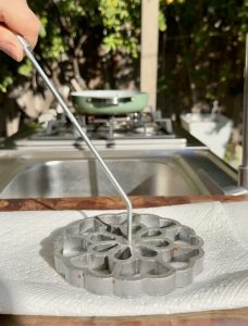 Hot rosette mold being tapped on a paper towel to remove excess oil.