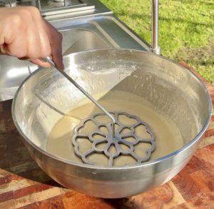 Rosette mold being dipped three quarters into buñuelos batter.