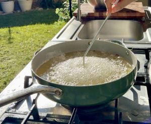 Batter-coated rosette mold entering hot oil to fry buñuelo.