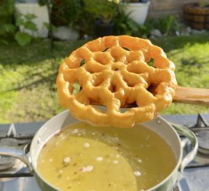 Fried buñuelo being lifted from oil and drained.