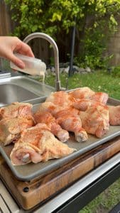 Smoked paprika being sprinkled over chicken pieces.