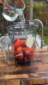 Water being poured into a blender with roasted tomatoes and white onion.